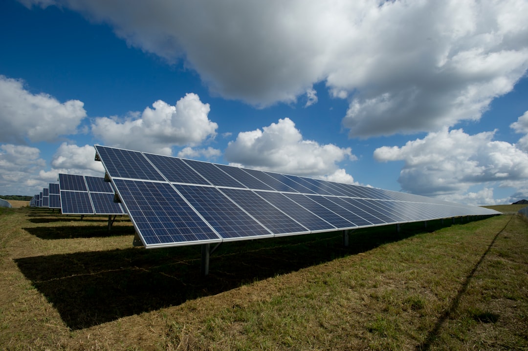 Rows of ground-mounted solar panels beneath a cloudy blue sky